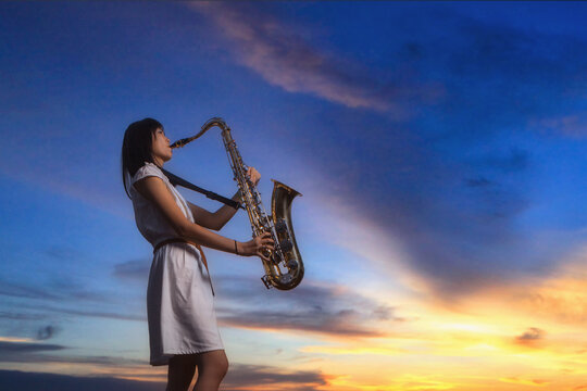 Side view of a female saxophonist standing in front of a dramatic sky playing the saxophone