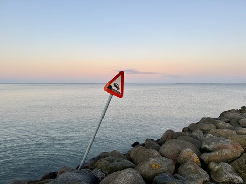 Leaning road sign warning of cars driving over the edge at sunset, Hou, Jutland, Denmark