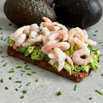 Close-up of an Open rye bread sandwich with avocado, prawn and chives on a kitchen worktop