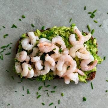 Close-up overhead view of an Open rye bread sandwich with avocado, prawn and chives on a kitchen worktop