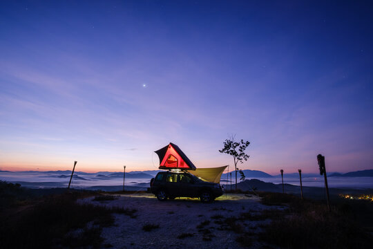 Side view silhouette of an illuminated off road vehicle with a tent on top parked on a mountain at sunset, Yan, Kedah, Malaysia