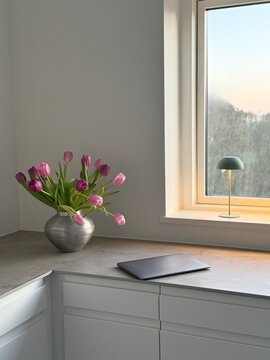Closed laptop computer on a kitchen counter next to a vase with pink tulips