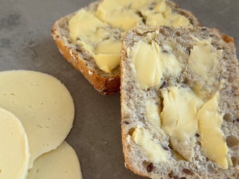 Close-up of a fresh bread roll with butter and sliced cheese on a kitchen worktop