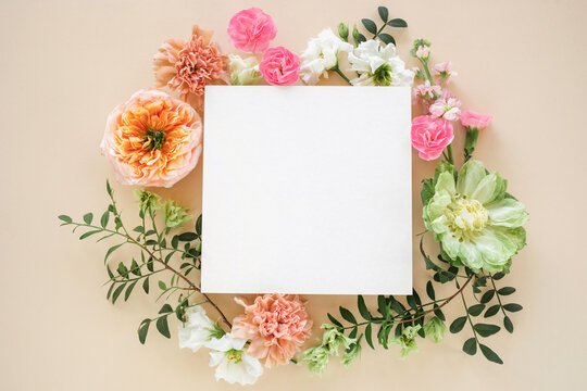 Close-up of a blank card in the middle of a Floral wreath made of peony-shaped roses, lisianthus, carnation flowers and pistachio twigs on a beige background