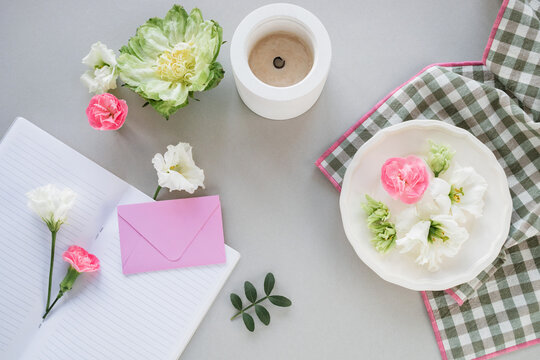 Close-up overhead view of assorted flowers, a candle, blank envelope and open notebook on a table