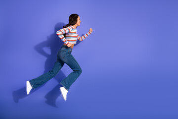Fototapeta premium Young woman running in a striped top jeans and white shoes against a purple background for lifestyle fitness and fashion stock photo