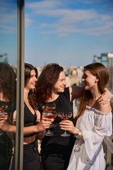 Naklejka premium Happy girlfriends making a toast with glasses of champagne on terrace outdoors