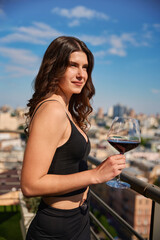 Naklejka premium Pretty young woman posing with red wine enjoying view on the terrace