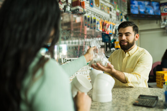 Hardware store clerk assisting a client with plumbing supplies, purchasing pipes and fittings at the checkout register