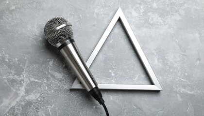A silver microphone rests diagonally against a gray background. A metallic geometric shape is next to it