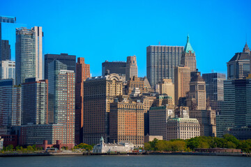 Obraz premium Dense urban landscape of the Lower Manhattan skyline featuring the historic Woolworth Building and modern skyscrapers under a clear blue sky, New York City.