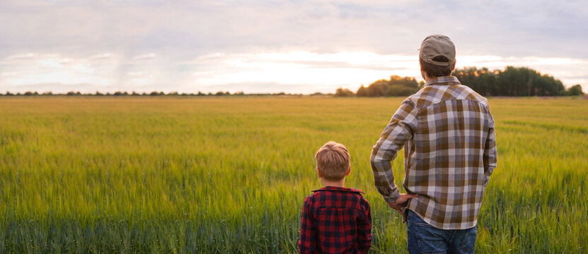Farmer and his son in front of a sunset agricultural landscape. Man and a boy in a countryside field. Fatherhood, country life, farming and country lifestyle concept.
