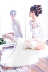 Seductive young beautiful woman with sexy legs in stockings and bridal lingerie posing in white vintage interior.
