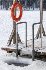 Fototapeta premium Hole in a frozen lake with wooden pier and lifesaver covered in snow ready for cold therapy, ice bathing. Wim Hof Method, cold therapy, breathing techniques, yoga and meditation