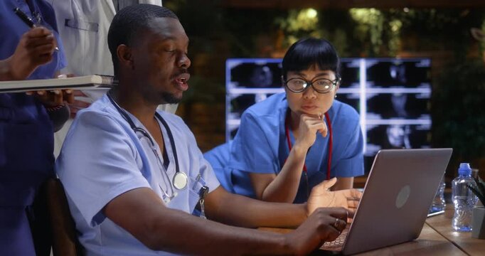 Multiethnic medical team analyzing patient data on a laptop during a clinical meeting, African male doctor and Asian female colleague discussing diagnosis using computer, healthcare collaboration.