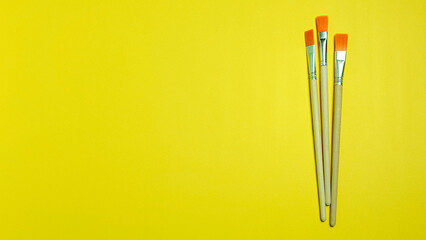 Three artist paint brushes arranged vertically on a solid yellow background with copy space
