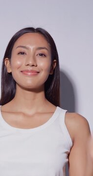 vertical clip. Beautiful Asian woman with tanned skin touching her face and smiling at camera.