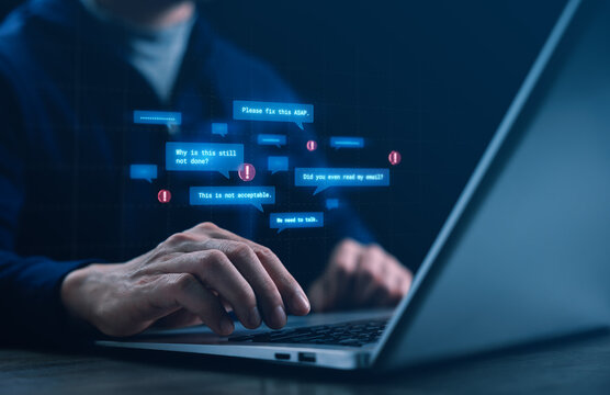 Hands typing on a laptop as hostile digital messages appear, representing workplace cyberbullying and toxic remote work, highlighting stress, conflict, and mental health issues in online offices.