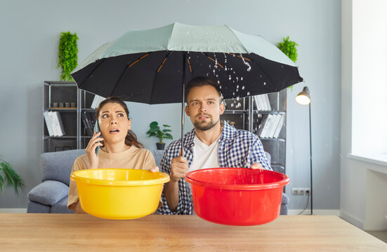 Phone call to repair service from woman, problem of couple due to roof damage, water leaking during rain. Man holding umbrella, plastic bucket and collecting falling drops from ceiling in living room