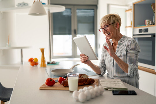 Joyful senior woman using tablet indoors in bright kitchen modern home morning work