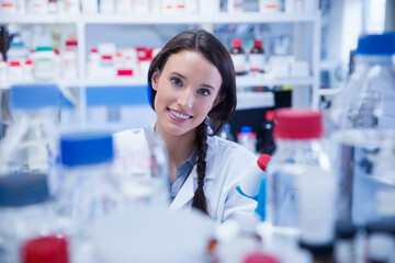 Clear reagent bottles and red wash bottle are lining lab bench with shelving and vials behind