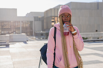 African American woman wearing pink beanie hoodie standing on rooftop sipping red drink, copy space