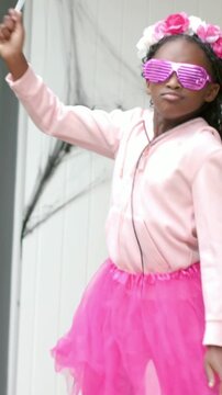Vertical video: Raising left arm, child performing for camera in pink hoodie and tutu, waving wand