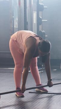 Vertical video: Adjusting grip, feet, woman lifting barbell at gym for strength, wearing pink tank