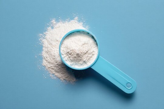 Blue measuring scoop filled with white powder on light blue background