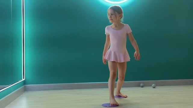 Young girl is practicing balance and coordination on gliding discs in fitness studio, training stability and body control