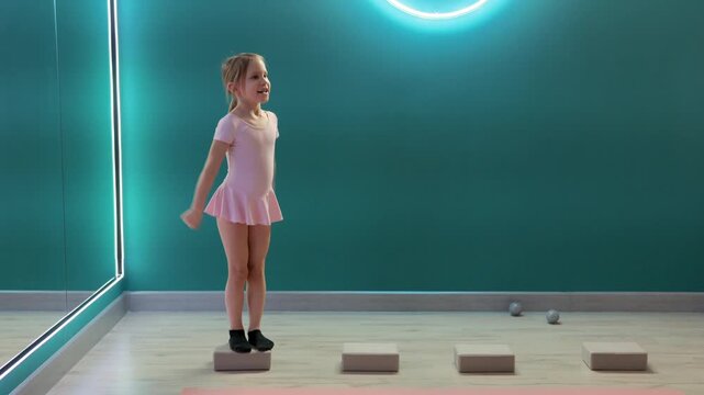 Young girl is stepping across foam blocks while tossing and catching ball in fitness studio, practicing balance, coordination, and agility