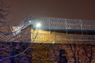 Mur więzienia z drutem kolczastym w nocy z lampą © FotoDax