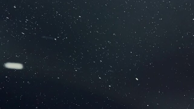 Night snowfall with glowing lens flare and soft bokeh. Gentle white flakes drift across dim urban light, subtle grain and green blue tint add cinematic, nostalgic atmosphere perfect