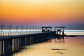 Obraz premium A breathtaking sunset over the Red Sea in Egypt, with a long wooden pier stretching across calm, reflective water.