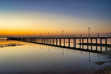 Fototapeta premium A breathtaking sunset over the Red Sea in Egypt, with a long wooden pier stretching across calm, reflective water.