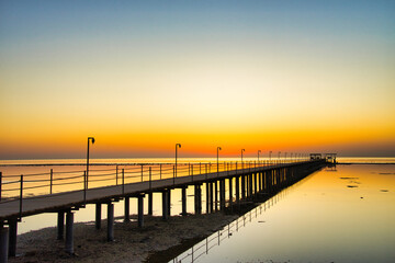 Obraz premium A breathtaking sunset over the Red Sea in Egypt, with a long wooden pier stretching across calm, reflective water.