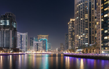 Obraz premium Geometry of modern desert cities with illuminated waterfront towers, layered facades and shimmering reflections defining contemporary marina skyline identity in Dubai at night.