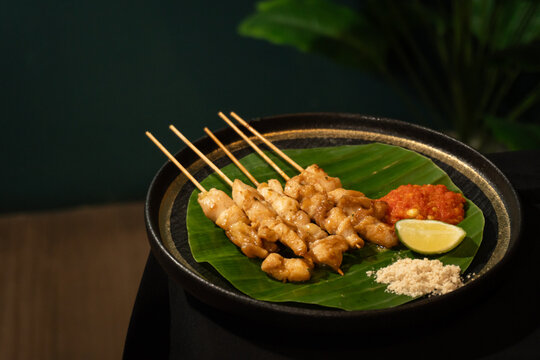 A plate filled with Indonesian sate taichan. Grilled chicken satay with spicy chili sauce and lime juice, lined with banana leaves.