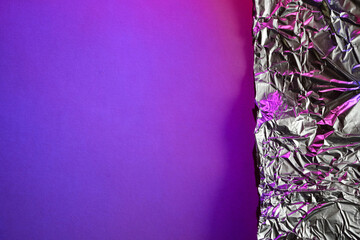 Crumpled metallic foil on vibrant purple background illuminated by neon pink light