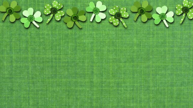 St Patricks Day top border of moving handmade paper button shamrocks. Stop motion loop video. Above view over a green linen background with copy space.