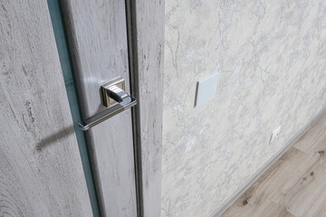 Modern interior with light grey textured wall, wooden-finish door, sleek metallic door handle,...