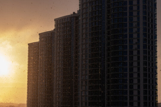Serene urban evening view with rainy glass and illuminated skyscraper silhouettes