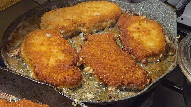 Frying traditional breaded pork chops or schnitzel in hot oil inside a pan, golden crispy meat cutlets cooking on stove, homemade dinner preparation process. Video 4K