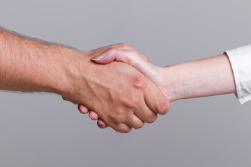 Close-up of a handshake between a man and a woman isolated on a gray background.