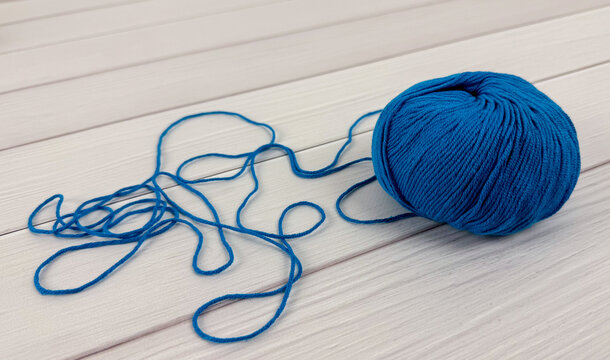 Blue yarn ball with loose strand on white wooden background