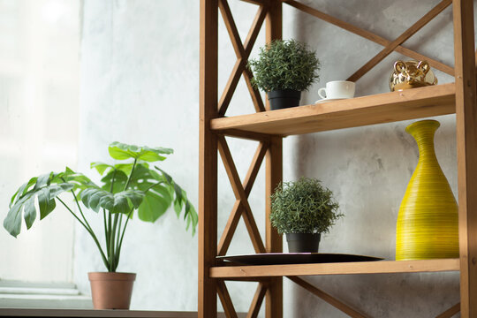 Modern interior detail featuring wooden shelving with potted plants, decorative vase, and ceramic cup against a textured wall and window backdrop