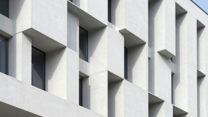 Fototapeta premium Modern concrete building facade with geometric window recesses and shadows