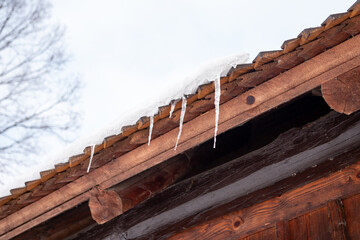 Icicles hanging from a wooden roof edge covered with snow. Winter detail of rural house showing frozen water and cold weather conditions.