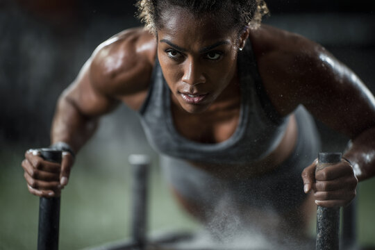 Black female power athlete performing heavy sled push. Explosive, sweat-driven functional strength training moment. Functional training gym, healthy lifestyle. Diversity theme.