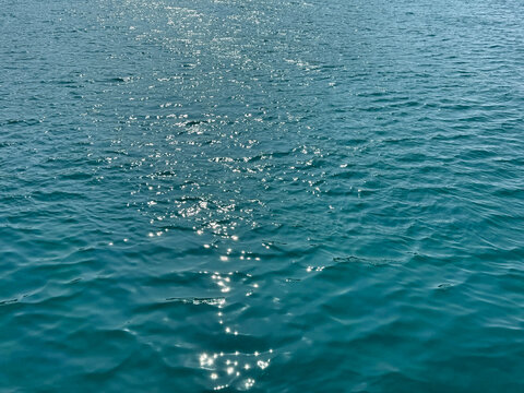 Blue ocean water with sun reflections sparkles on surface.